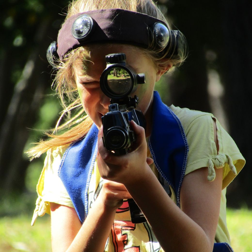 A girl in camo face paint looks down the scope of her laser tag rifle