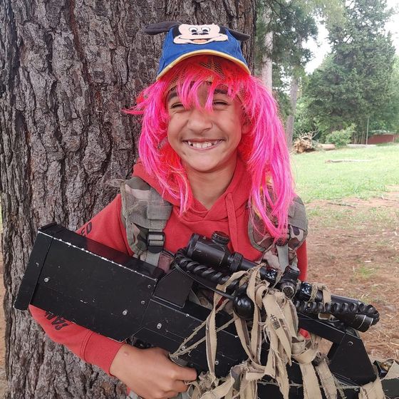 A girl in a pink wig behind a tree